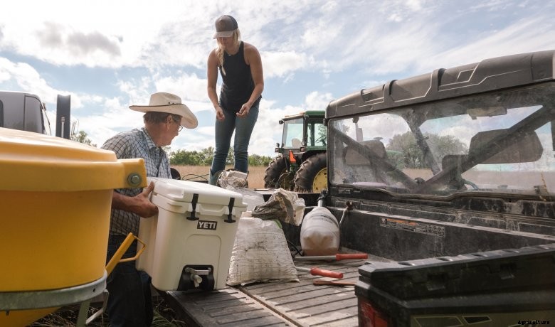 A farmer hands a white YETI Silo water cooler to a fellow farmer